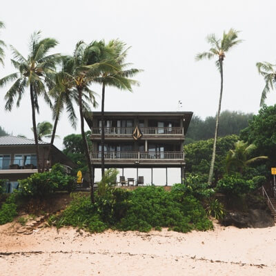 A view of a house from the beach, surrounded by palm trees